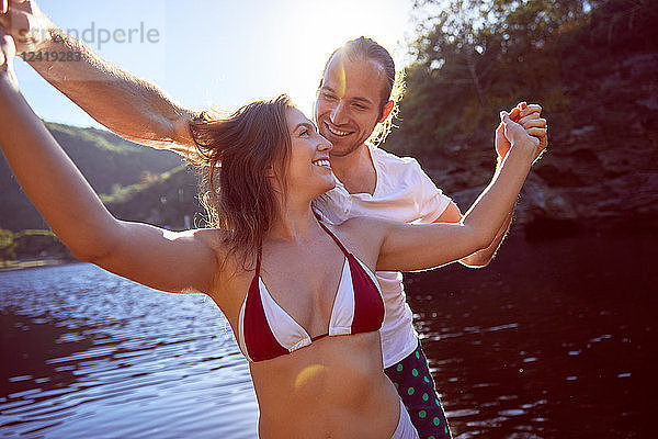 Happy  carefree couple holding hands at sunny summer lake