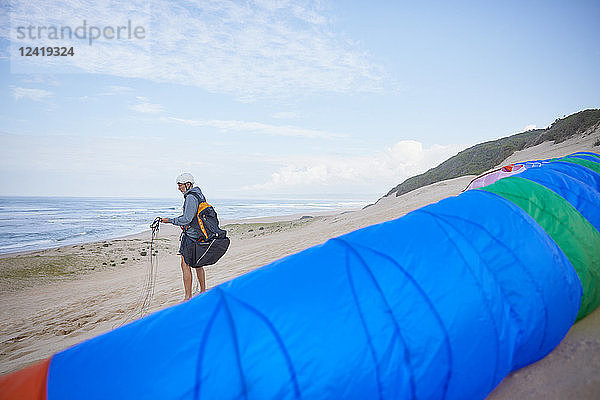 Male paraglider with parachute on ocean beach
