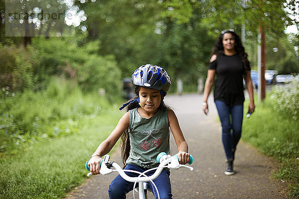 Mother watching daughter bike riding on path
