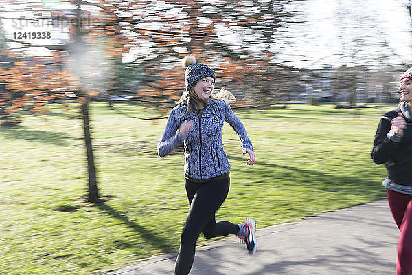 Smiling  confident female runner running in sunny park