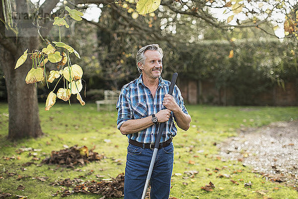 Lächelnder älterer Mann beim Harken von Herbstblättern im Hinterhof