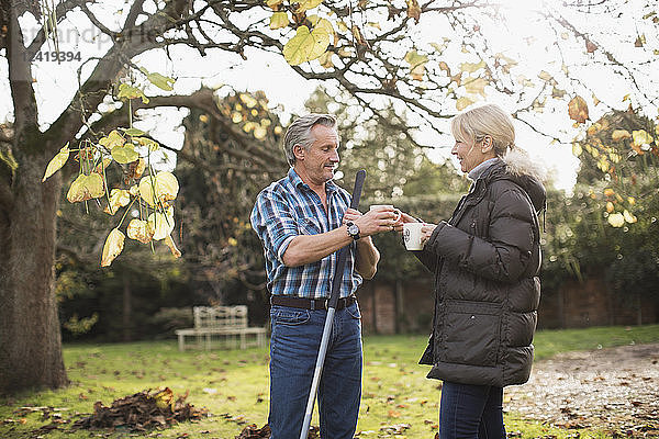Älteres Paar trinkt Kaffee und harken Herbstblätter in sonnigen Hinterhof