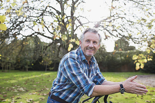 Porträt selbstbewusster älterer Mann  der im Herbst den Rasen im Hinterhof mäht