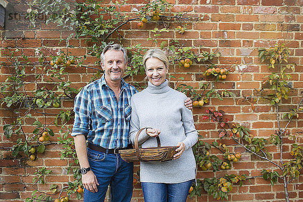 Porträt lächelndes reifes Paar beim Ernten von Äpfeln im Garten