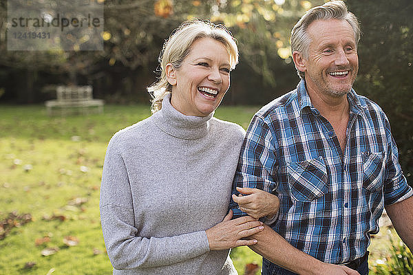 Glückliches  sorgloses reifes Paar  das Arm in Arm in einem sonnigen Herbstpark spazieren geht