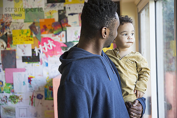 Vater hält neugierigen  unschuldigen Babysohn und schaut aus dem Fenster