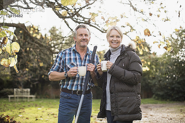 Lächelndes reifes Paar trinkt Kaffee und harken Herbstblätter im Garten