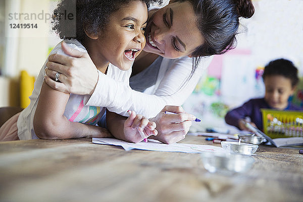 Liebevolle  glückliche Mutter umarmt Kleinkind Tochter Färbung am Tisch