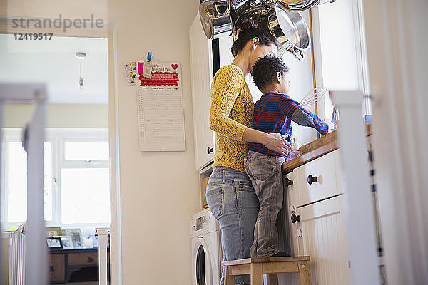 Mutter und kleiner Sohn auf einem Hocker beim Abwaschen in der Küche