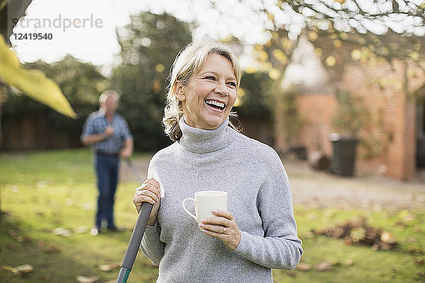 Glückliche reife Frau trinkt Kaffee und harken Herbstblätter im Hinterhof