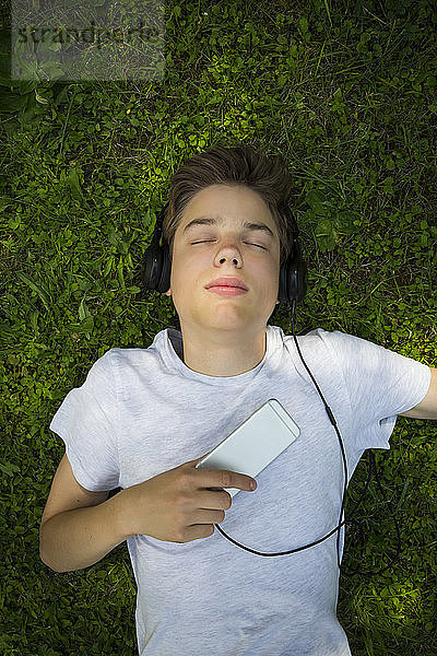 Portrait of boy lying on meadow listening music with headphones and smartphone