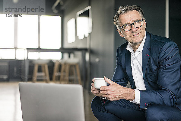 Smiling mature businessman with cup of coffee thinking