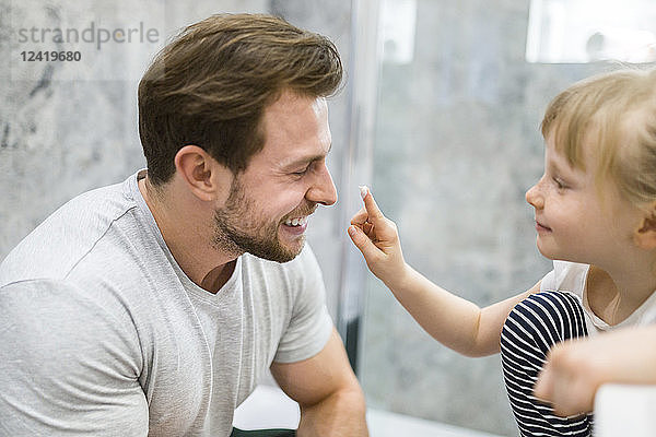 Father and daughter using face cream in bathroom