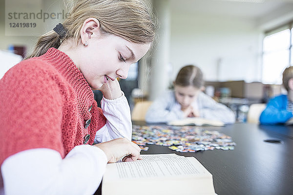 Schoolgirl reading book on table in school break room