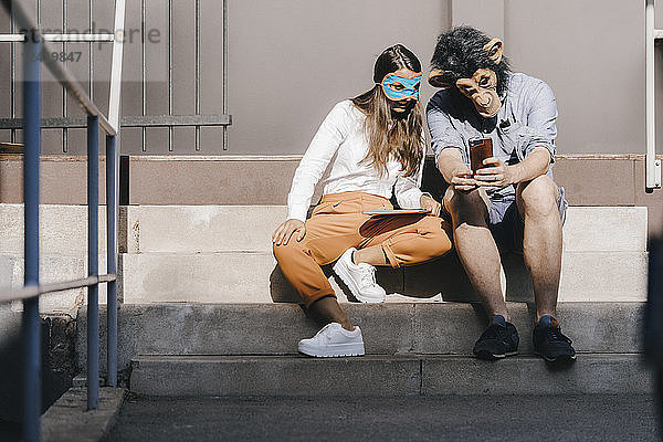 Couple in disguise sitting on stairs  using smartphone