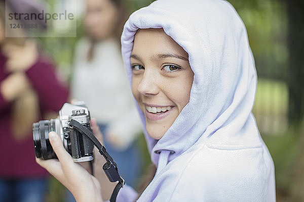 Portrait of smiling teenage girl with camera outdoors