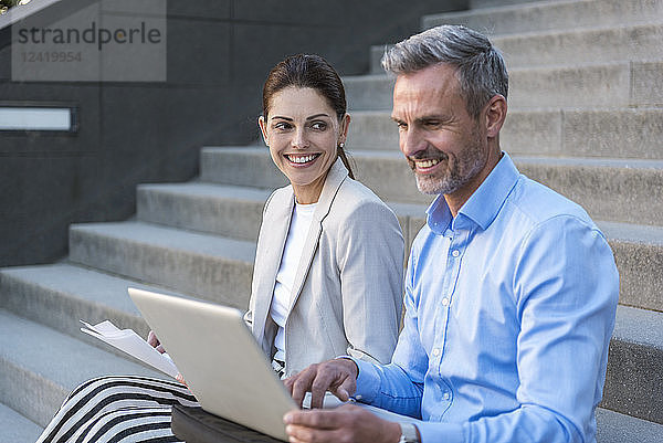 Two business people sitting side by side on stairs working together