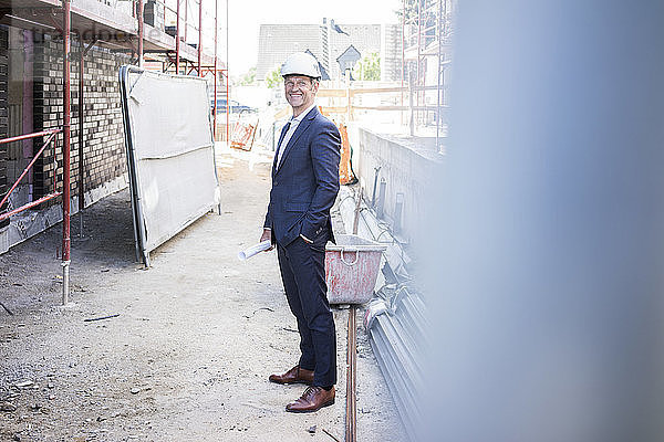 Smiling architect wearing hard hat standing on construction site