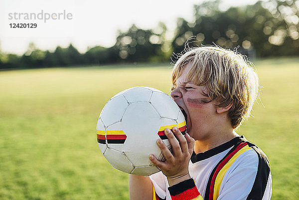 Boy with face paint and German football shirt  biting soccer ball