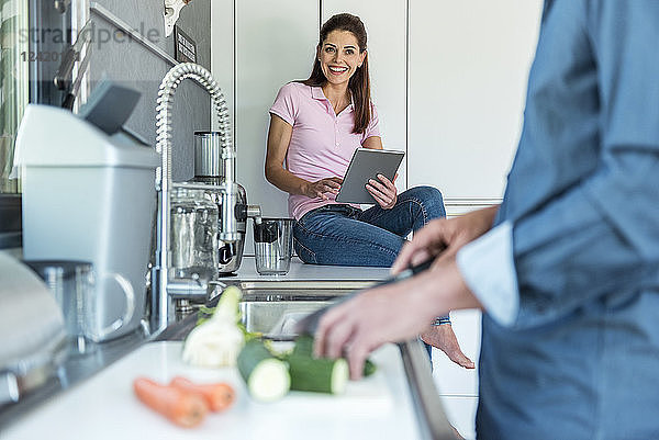 Happy couple in kitchen at home cooking and using a tablet