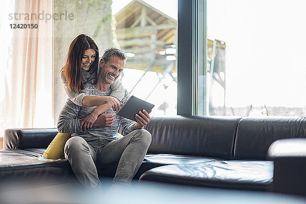 Happy couple on couch at home sharing a tablet