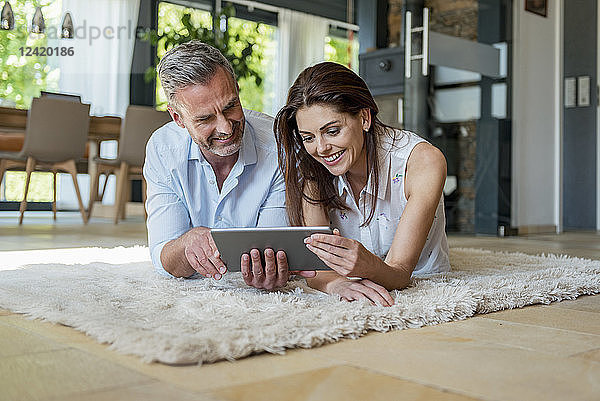 Happy couple lying on carpet at home sharing a tablet