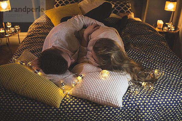 Romantic young couple cuddling in bed with fairy lights