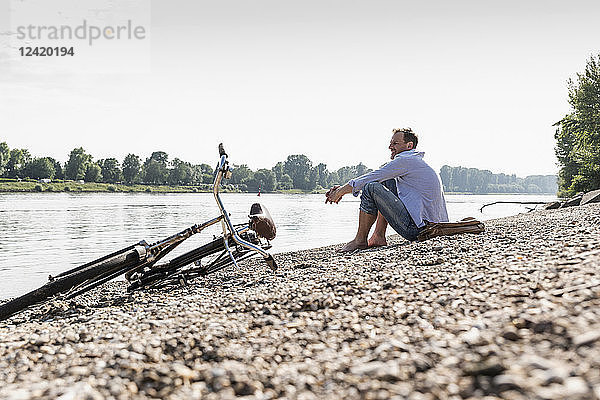 Mature man with bike sitting at Rhine riverbank