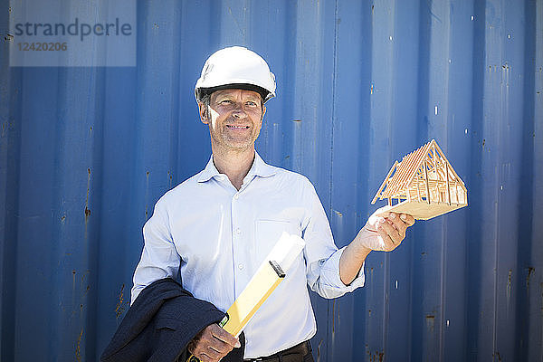 Smiling architect wearing hard hat holding house model