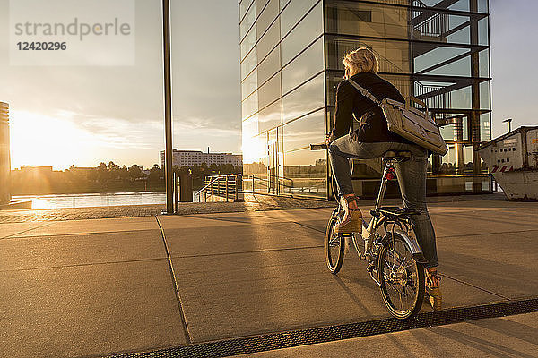 Senior woman with city bike at the riverside at sunset