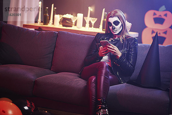 Bored woman using mobile phone at Halloween party