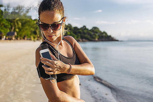 Thailand  Koh Phangan  Sportive woman during workout on the beach  smartphone