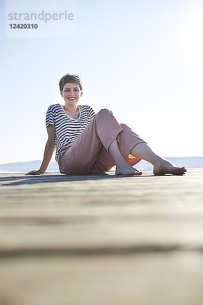 Smiling woman sitting on jetty at lake