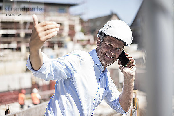 Smiling man wearing hard hat on cell phone on construction site