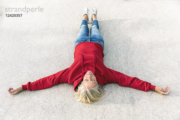 Senior woman wearing red hoodie lying on the ground outdoors