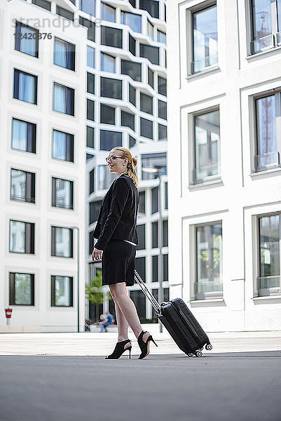 Mature businesswoman with suitcase walking in front of office buildings
