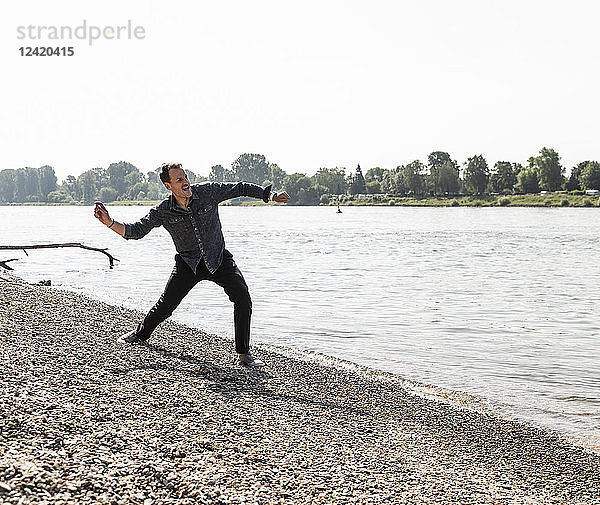 Mature man throwing stone at Rhine riverbank
