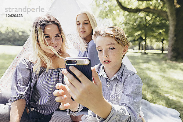 Two young women and a boy taking a selfie next to teepee in a park