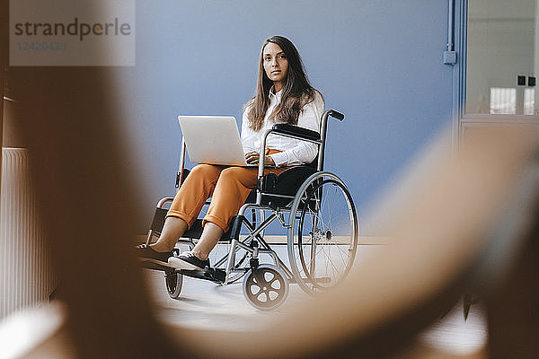 Young handicapped woman sitting in wheelchair  using laptop