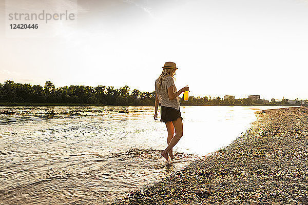 Young woman walking barefoot on riverside in the evening