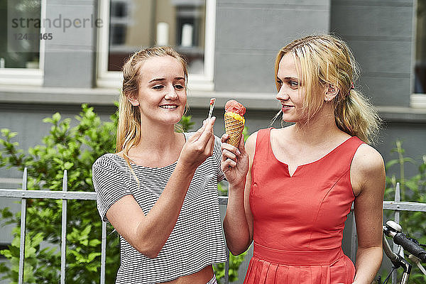 Two young women sharing an ice cream cone in the city