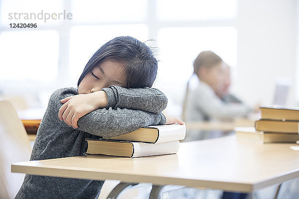 Schoolgirl sleeping on stack of books on table in school