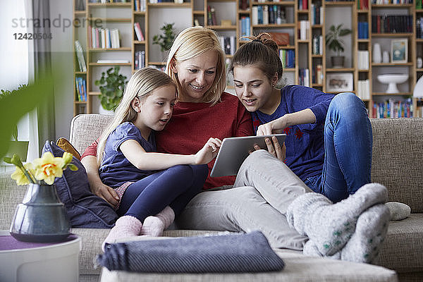 Mother and her daughters sitting on couch  having fun using digital laptop