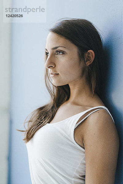 Young woman leaning against wall  looking at distance