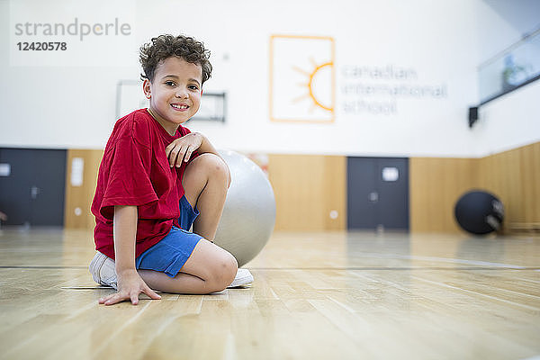 Portrait of smiling schoolboy with gym ball in gym class