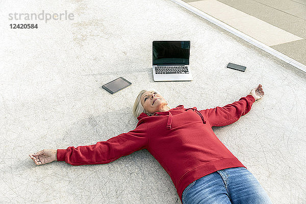 Senior woman wearing red hoodie lying on the ground next to mobile devices