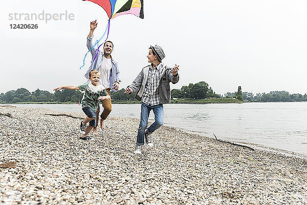 Happy father with two sons flying kite at the riverside