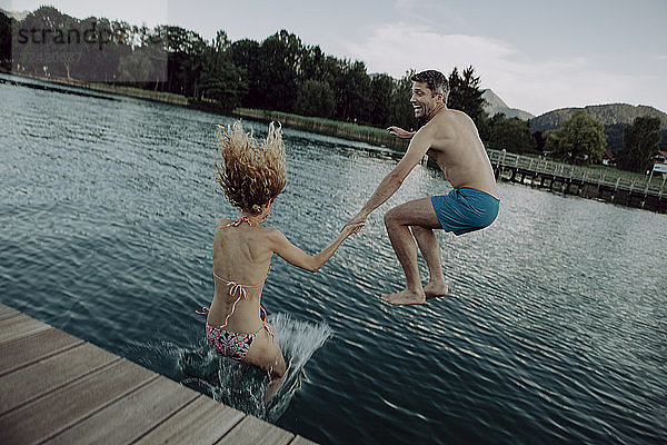 Happy couple jumping hand in hand into swimming lake