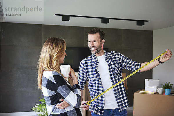 Couple moving into new flat measuring with tape measure