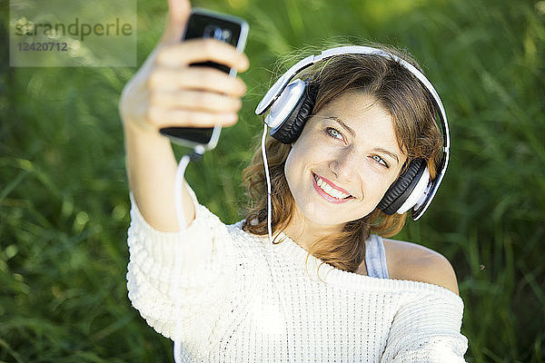Smiling young woman with earphones taking a selfie